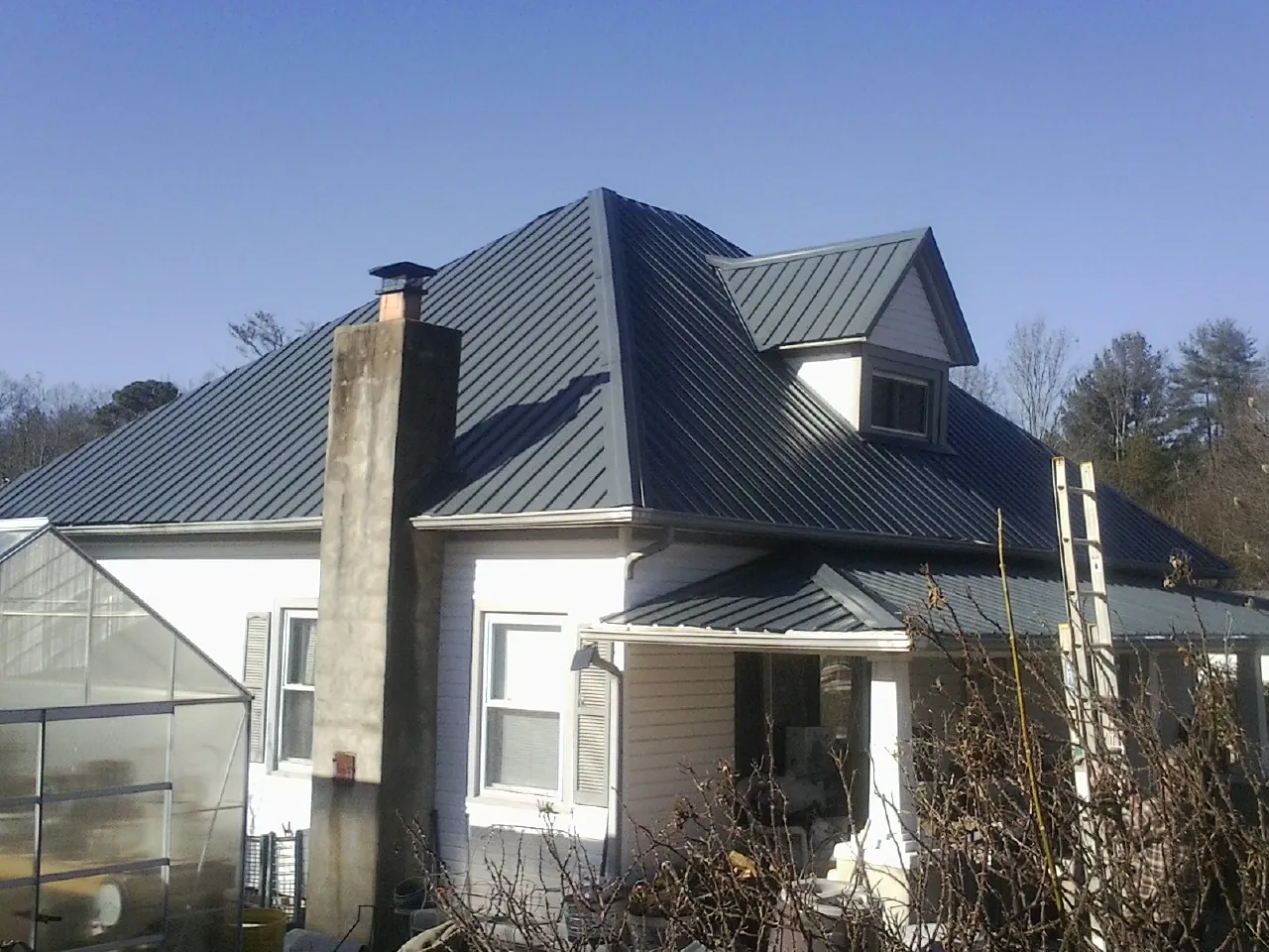 Dark blue standing seam metal roof on a white farmhouse with dormer — Slate & Tile Roof Repair by Roofing Brothers in Peconic