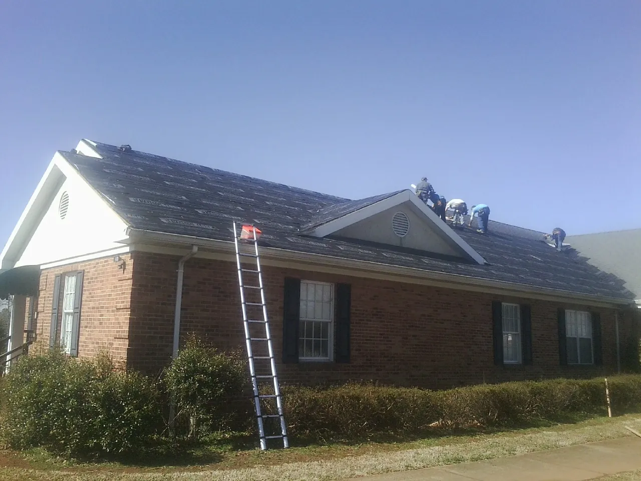 Crew tearing shingles off a brick ranch roof with a ladder set — Emergency Roof Repair work by our crew in Peconic