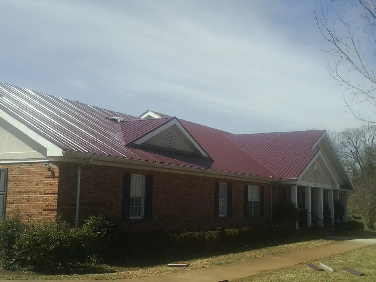 Red metal roof with gabled entries on a long brick building, from a Hail Damage Roof Repair job in Peconic