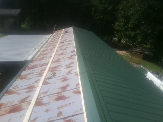 Old rusted panels beside newly installed green metal roofing — Wind Damage Roof Repair by Roofing Brothers in Peconic