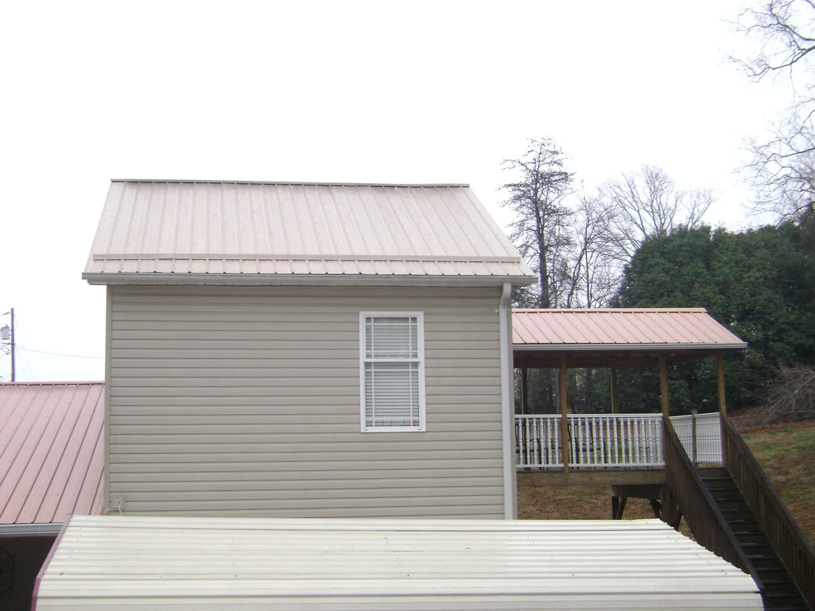 Tan metal roofs on a two story addition and attached porch, from a Roof Replacement job in Peconic